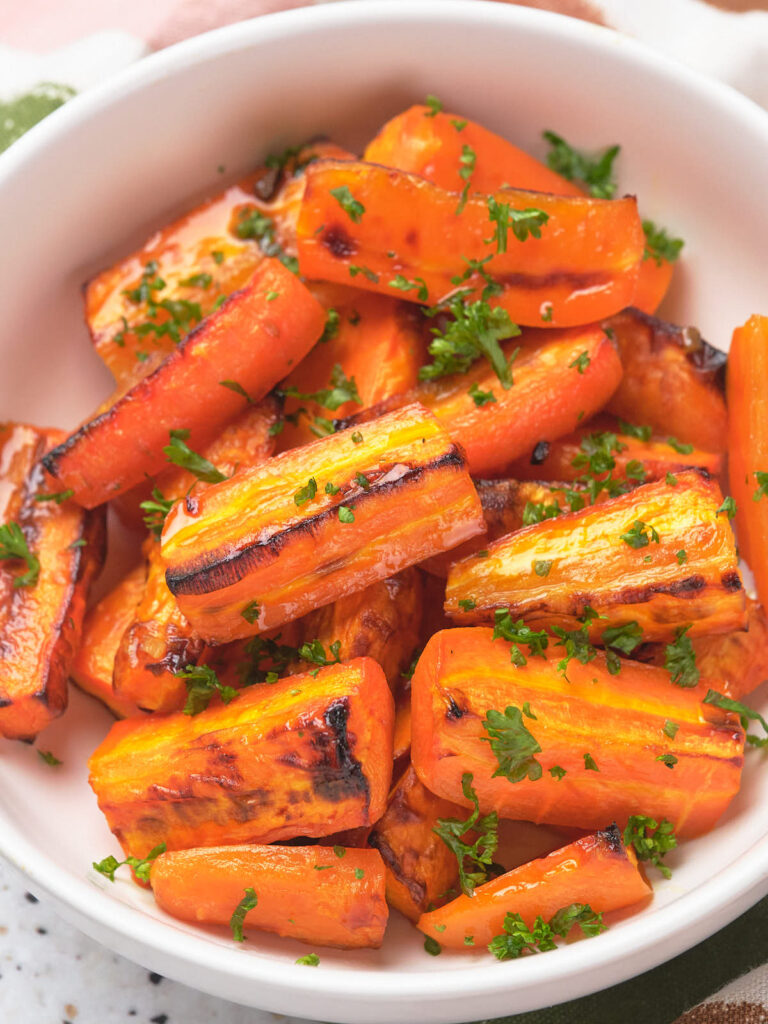 A bowl of honey roasted carrot pieces garnished with chopped parsley.