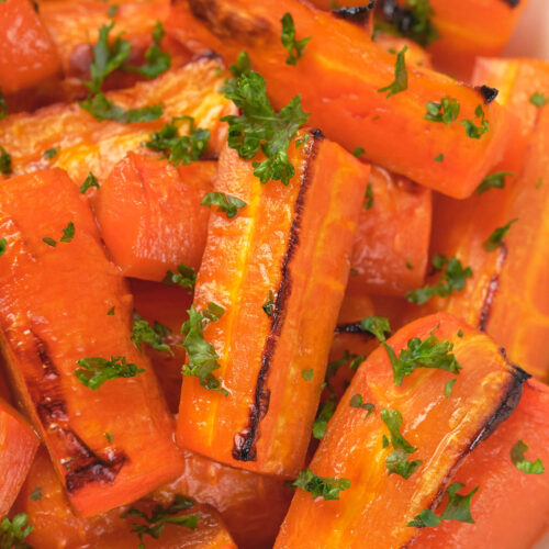Close-up of honey roasted carrot pieces with char marks, garnished with chopped parsley.