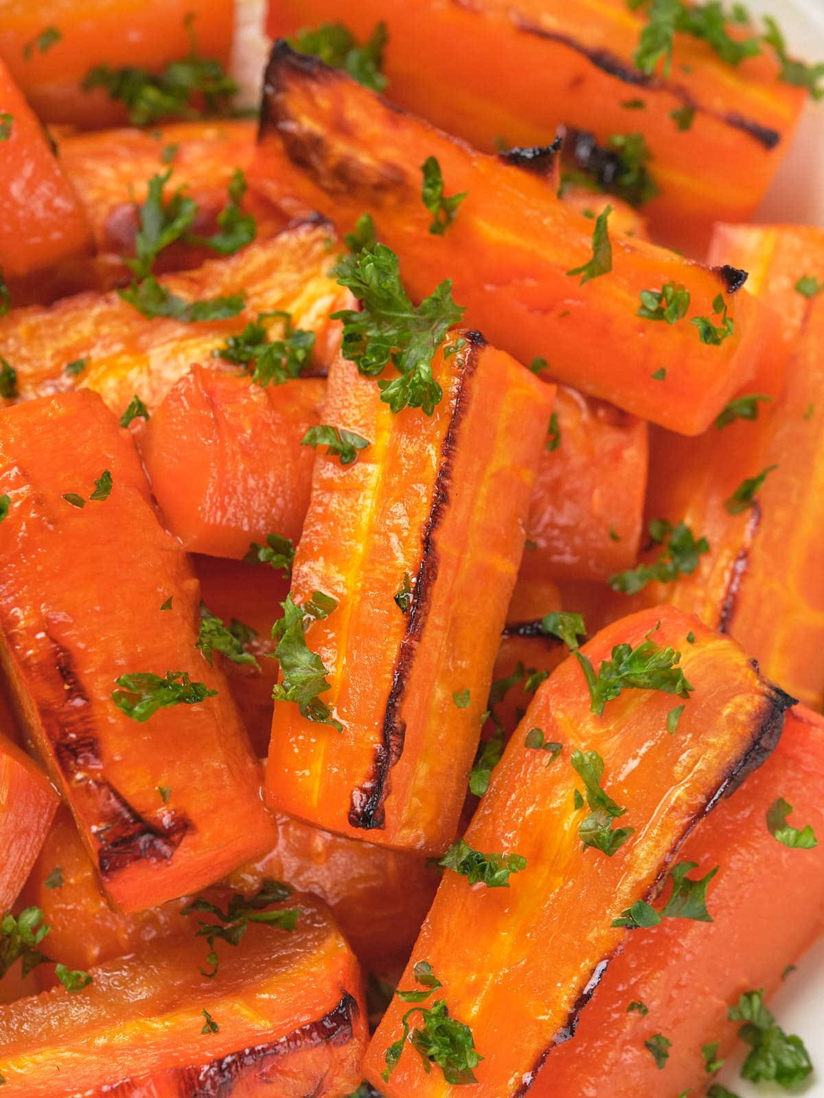 Close-up of honey roasted carrot pieces with char marks, garnished with chopped parsley.