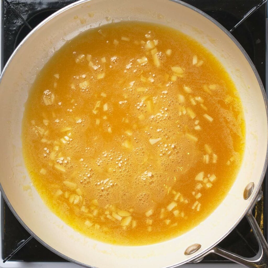 A saucepan on a stove containing a bubbling yellow sauce with chopped garlic.