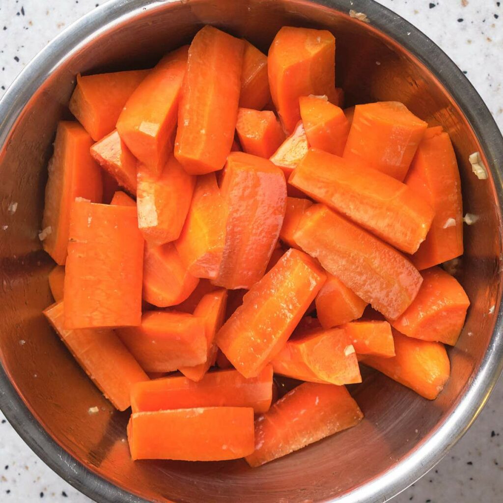Chopped orange carrots in a metal bowl on a speckled countertop.