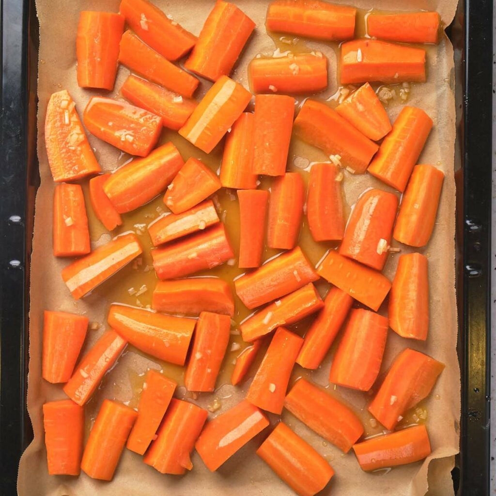 Chunks of carrots coated in oil and seasonings on a baking tray lined with parchment paper.