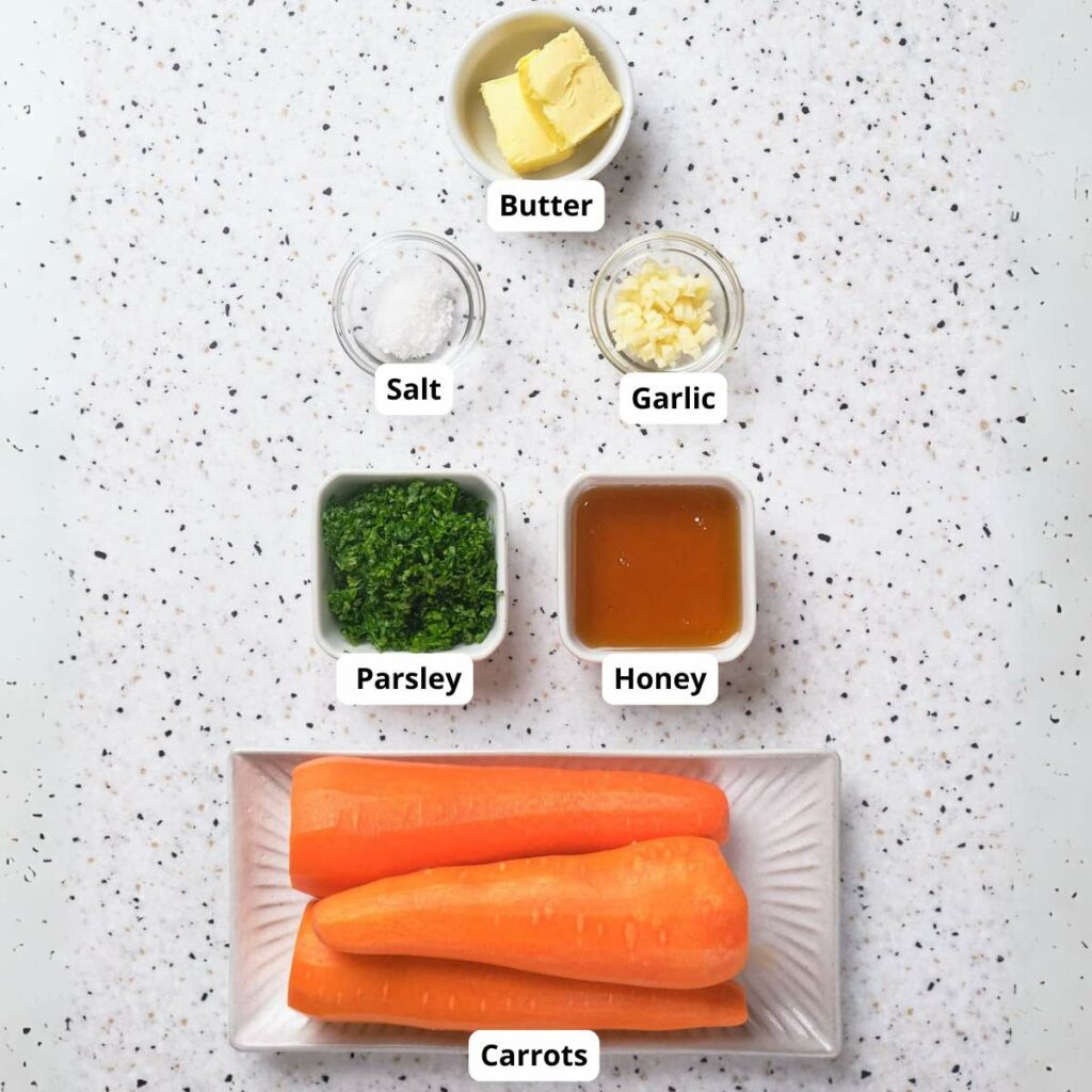 Ingredients on a speckled surface: butter, garlic, honey, parsley, salt, and three peeled carrots on a tray.