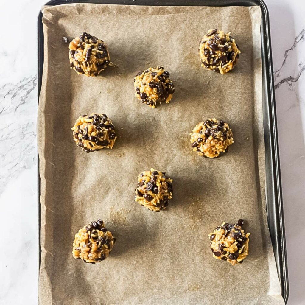 Eight cookie dough balls with chocolate chips on a parchment-lined baking sheet.