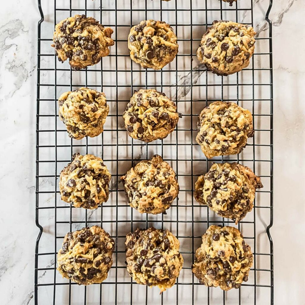 Twelve chocolate chip cookies cooling on a wire rack on a marble surface.