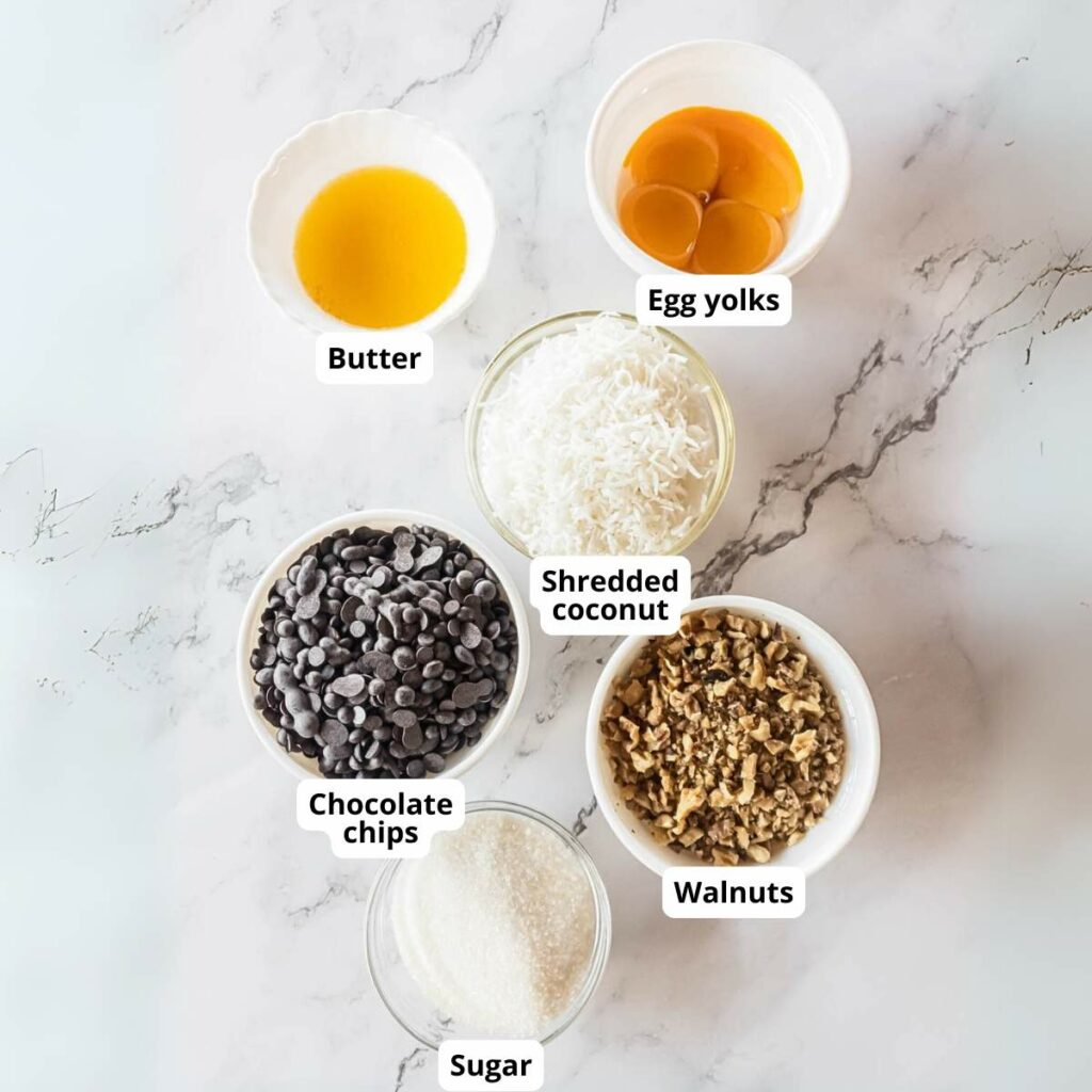 Ingredients for keto magic cookies on a marble surface:, each labeled in separate bowls.