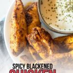 A plate of spicy blackened chicken tenders served with a bowl of creamy white dipping sauce, garnished with herbs.
