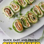 A plate of cucumber roll ups filled with cream cheese, smoked salmon, and herbs, sliced and arranged neatly on a white platter.