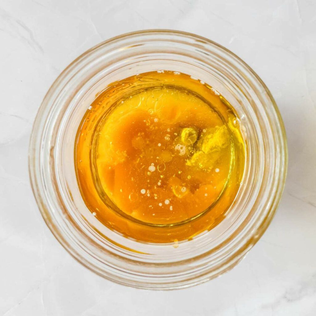 A glass bowl containing raw eggs and oil, viewed from above on a white surface.