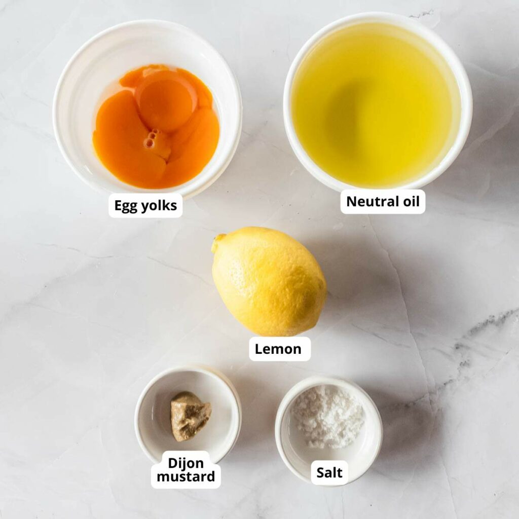 Five labeled ingredients for mayonnaise on a white surface.