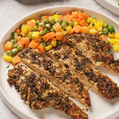 Pan seared chicken breast on a plate with mixed vegetables including corn, peas, carrots, and beans.