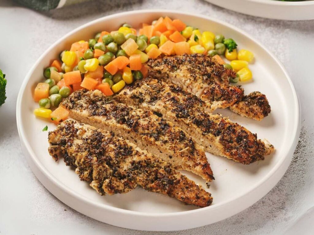 Pan seared chicken breast with a side of mixed vegetables, including peas, carrots, and corn, on a white plate.