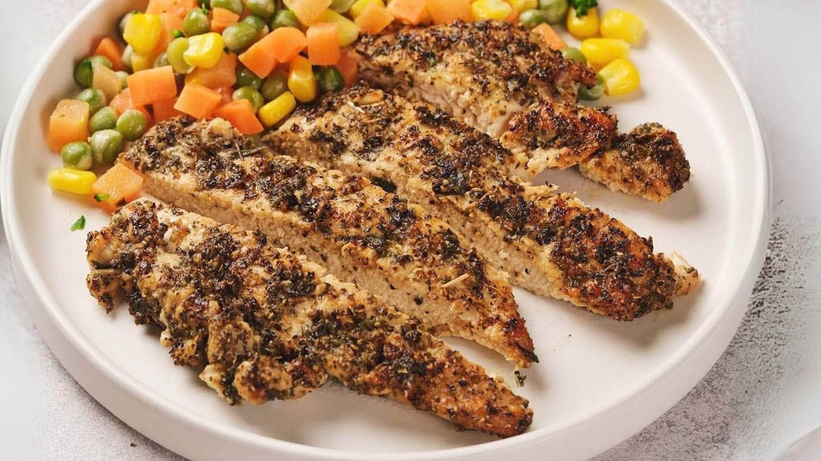 Pan seared chicken breast served with a side of mixed vegetables, including corn, carrots, and edamame, on a white plate.