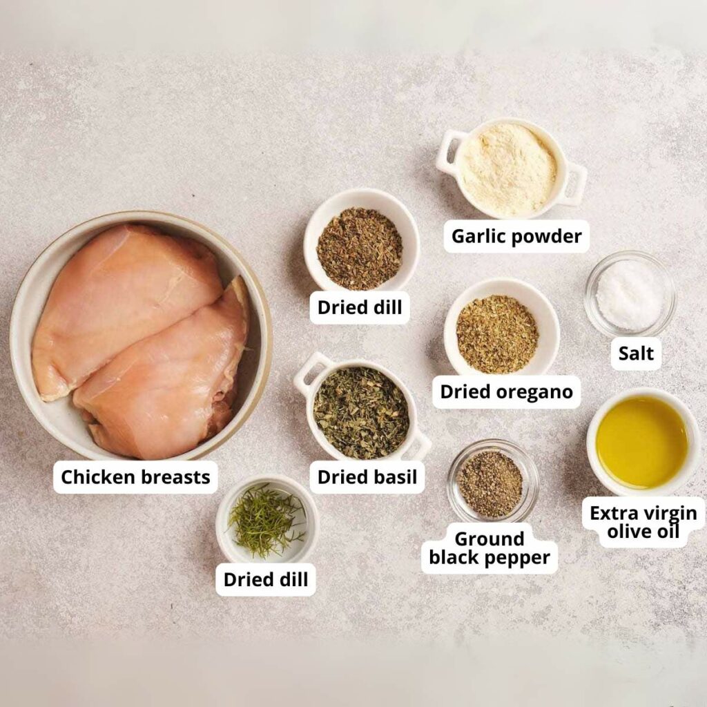 Raw chicken breasts and small bowls of garlic powder, salt, dried dill, oregano, basil, black pepper, and olive oil.