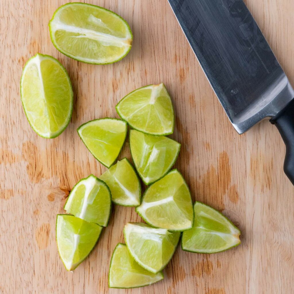 A cutting board with several lime wedges and a large kitchen knife.