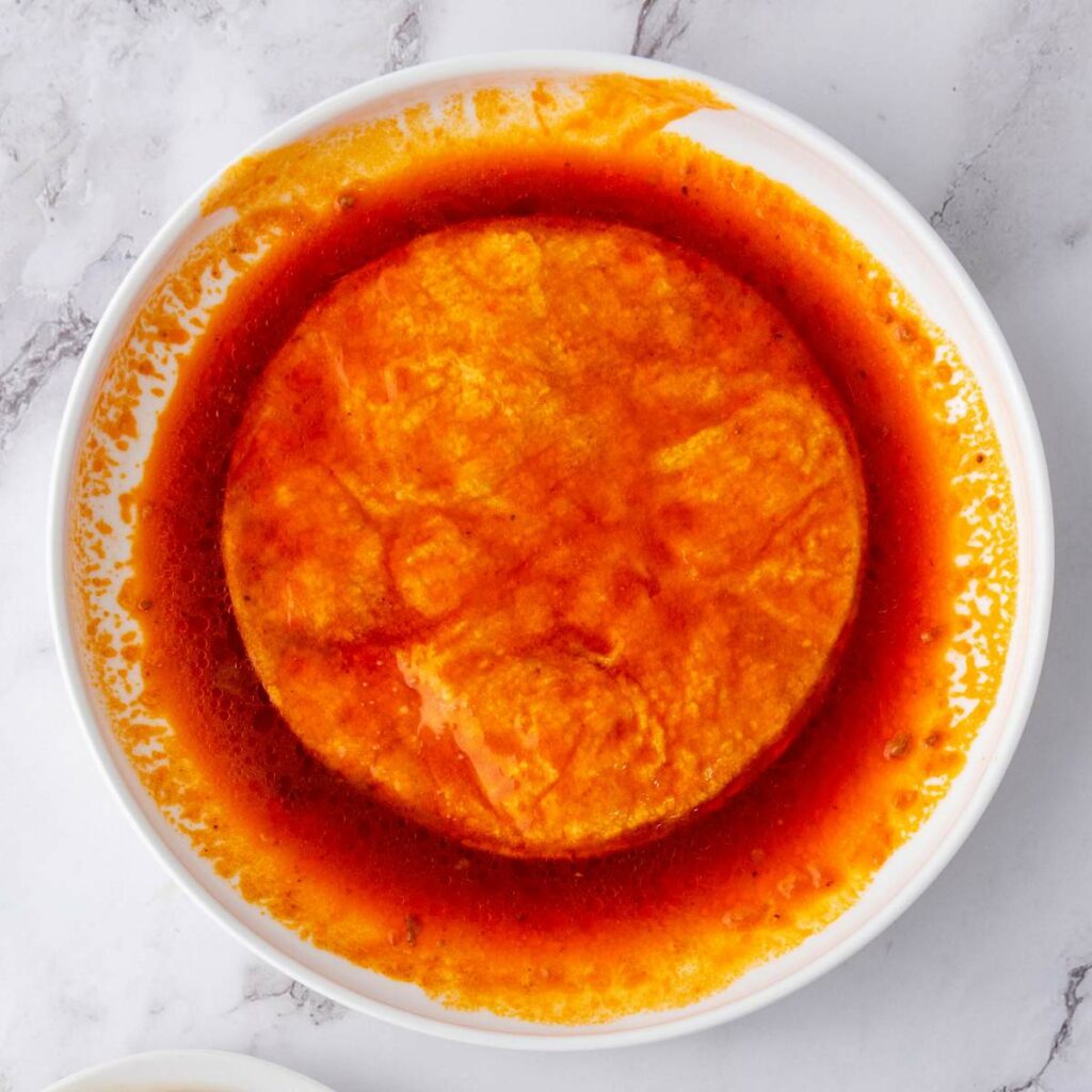 A white bowl containing a round serving of amala covered in red, oily stew sits on a marble surface.
