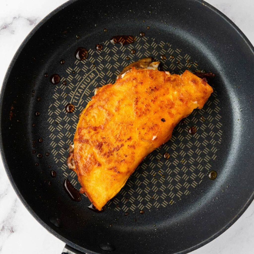 A folded, golden-brown taco is being cooked in a black frying pan with a patterned base.