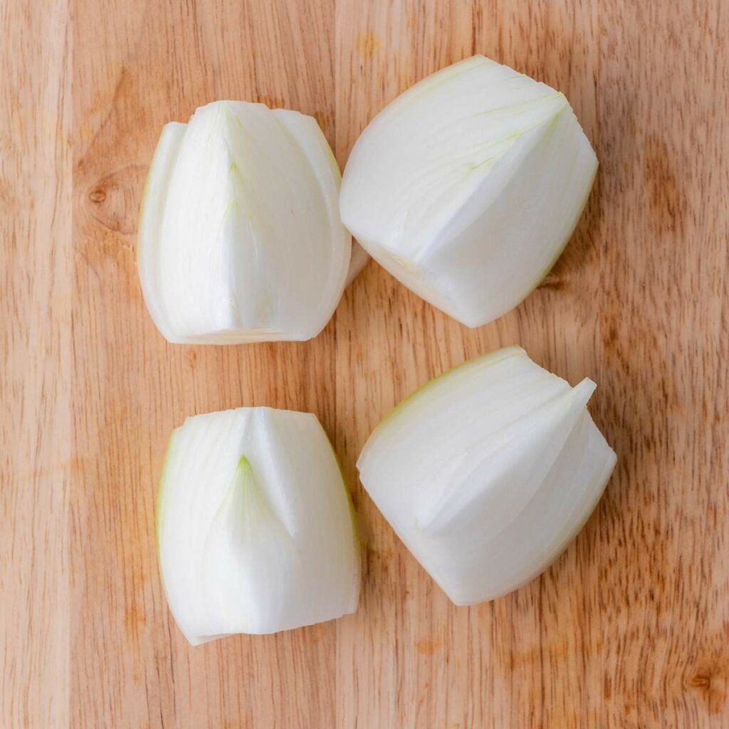 Four white onion quarters arranged on a wooden cutting board.