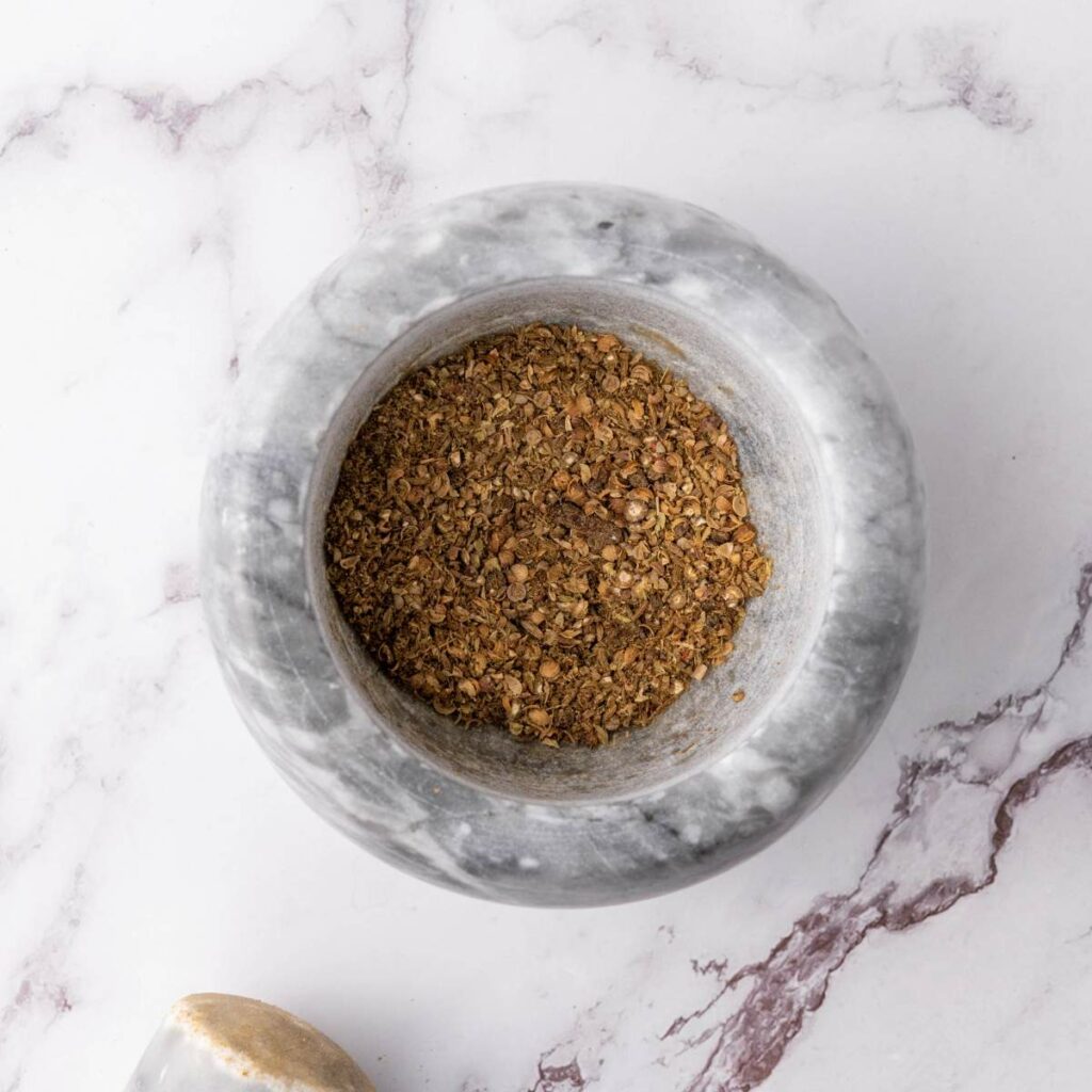 Ground spices in a gray marble mortar on a white marble surface, viewed from above.