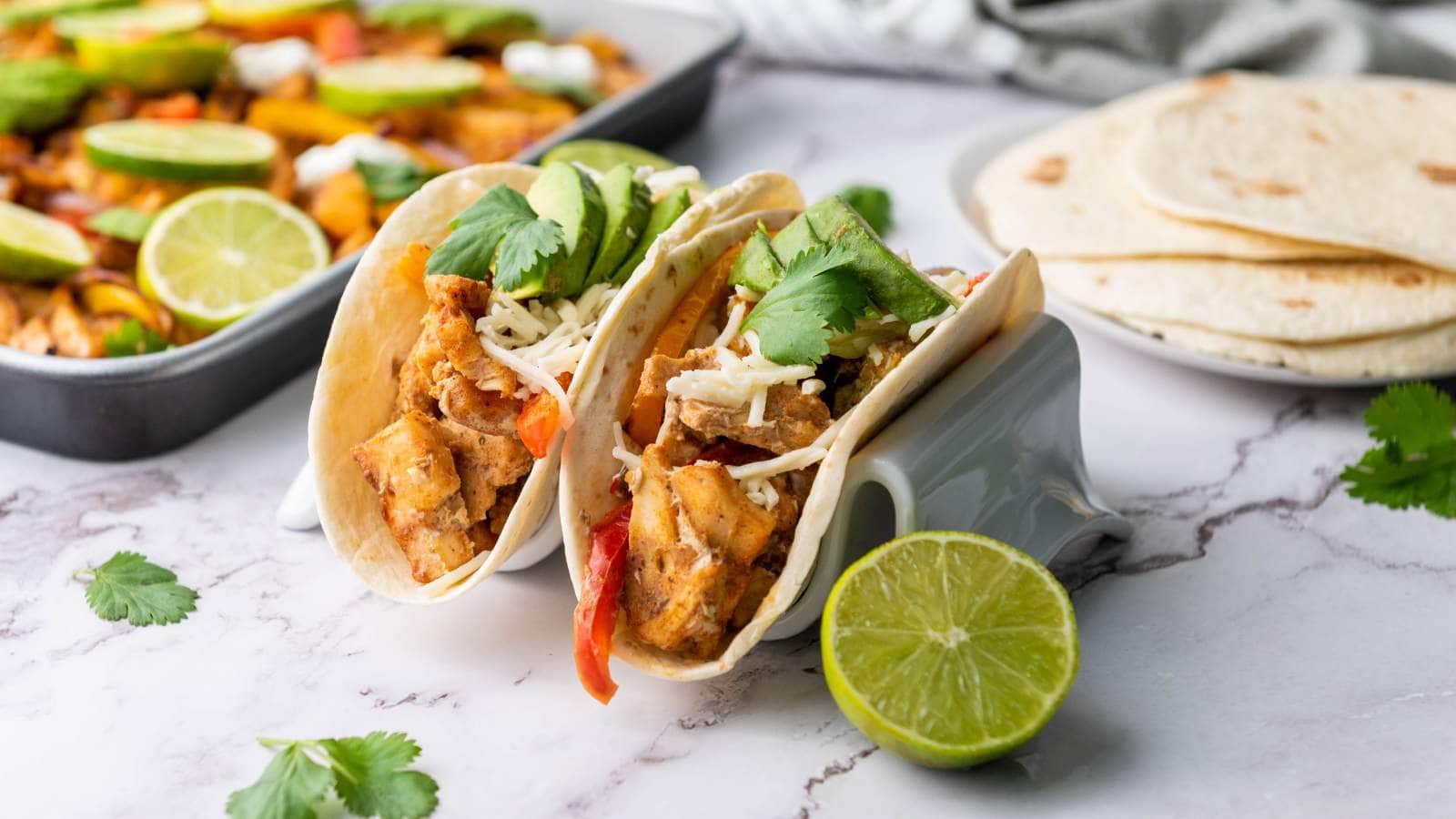 Two chicken fajitas with shredded cheese, avocado slices, and cilantro in taco holders.