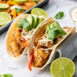 Two chicken fajita tacos with avocado, cheese, cilantro, and peppers on tortillas.