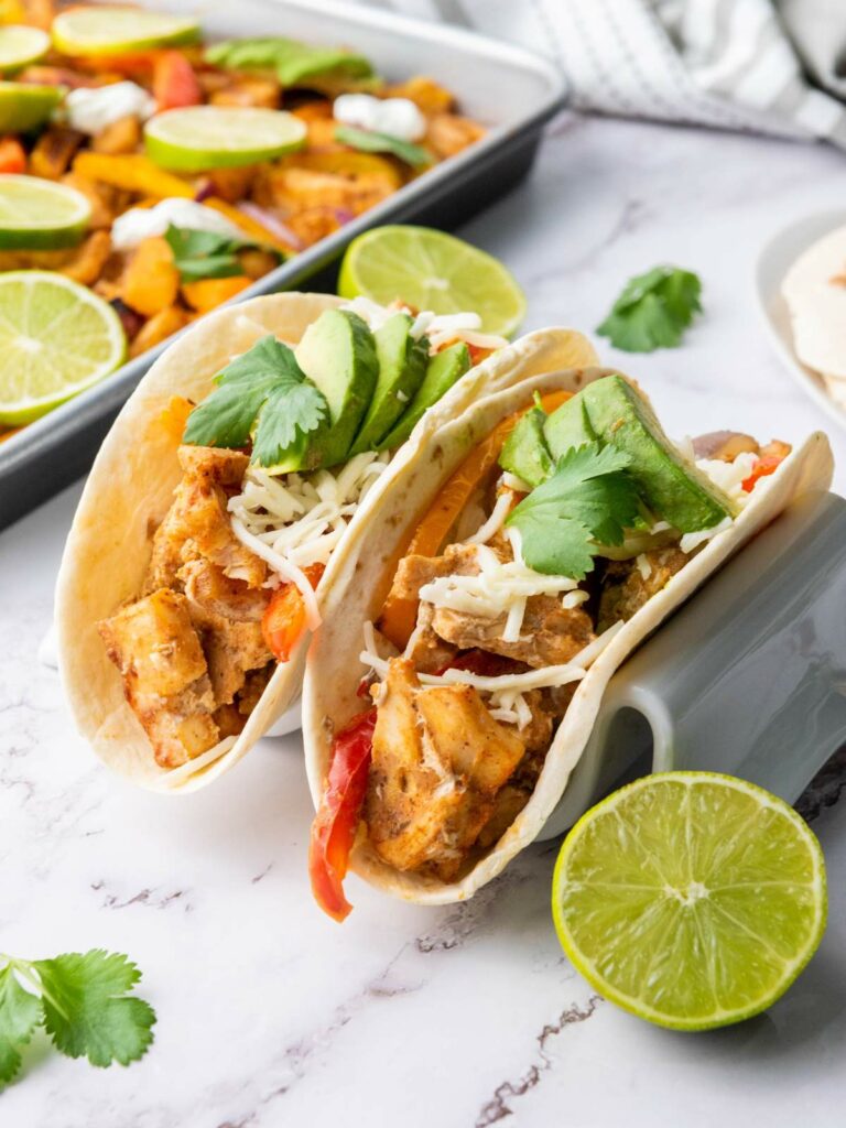 Two chicken fajita tacos with avocado, cheese, cilantro, and peppers on tortillas.