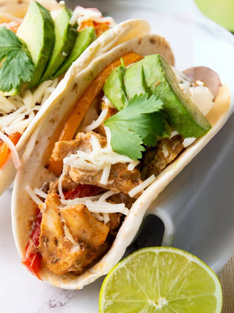 A close-up of a chicken fajitas with shredded cheese, seasoned chicken, avocado slices, cilantro, and bell peppers.