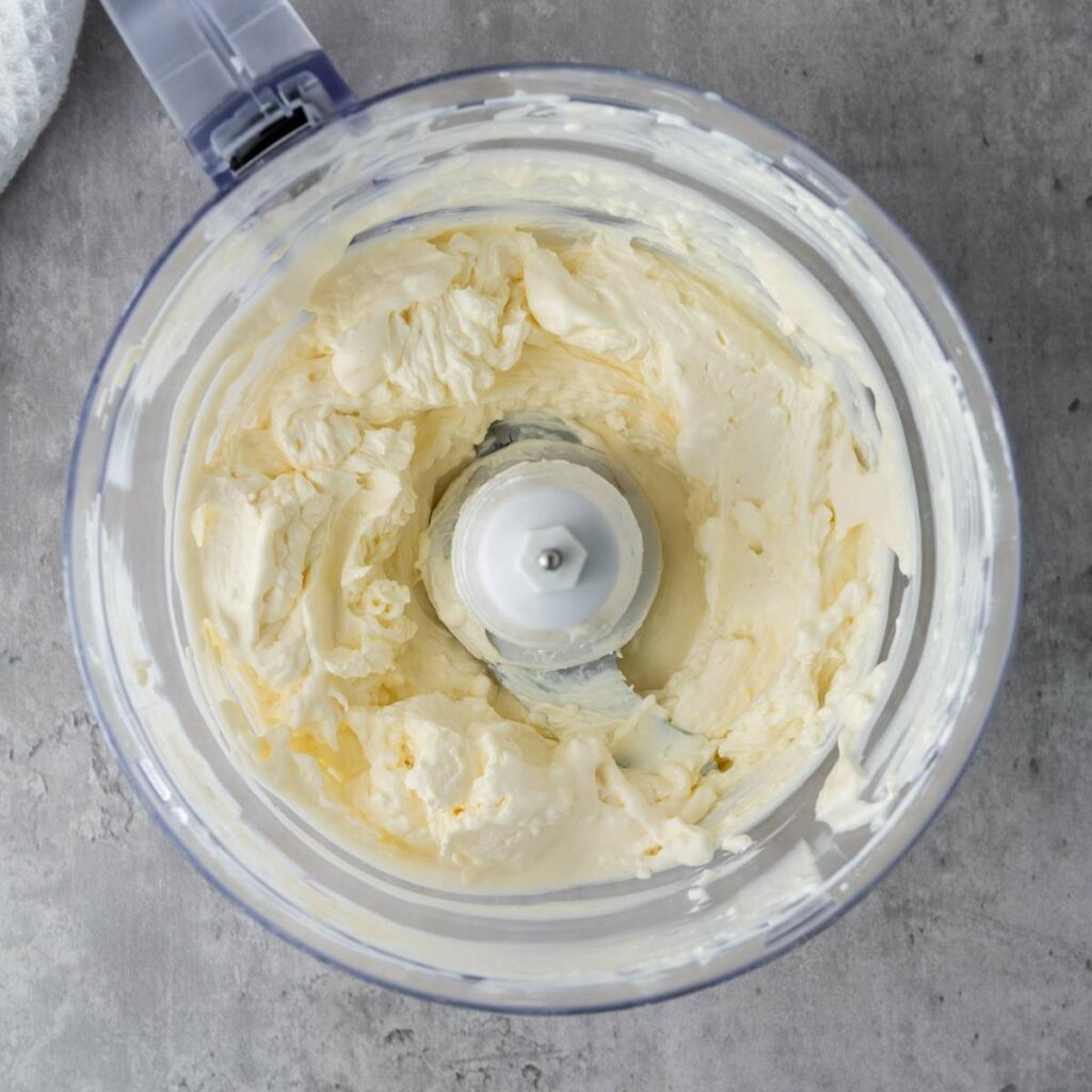 A food processor containing smooth, creamy butter on a gray countertop.