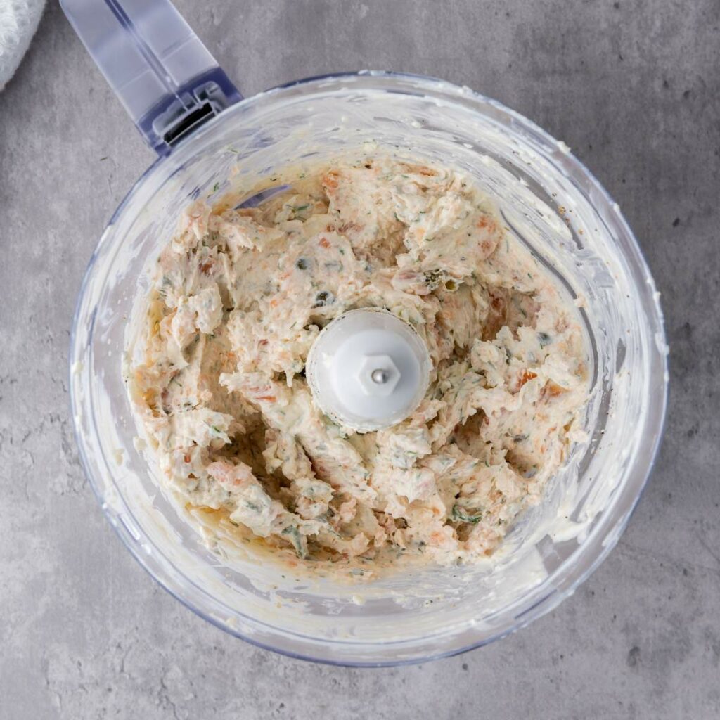 A food processor containing a mixture of chopped ingredients, including herbs, sits on a gray countertop.