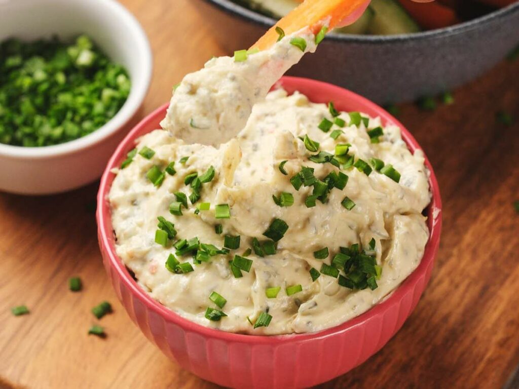 A pink bowl filled with sour cream dip, topped with chopped green herbs.
