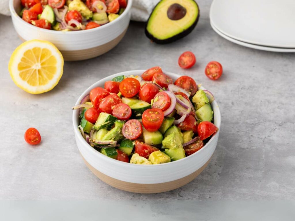 A bowl of avocado tomato salad with cucumber sits on a table.