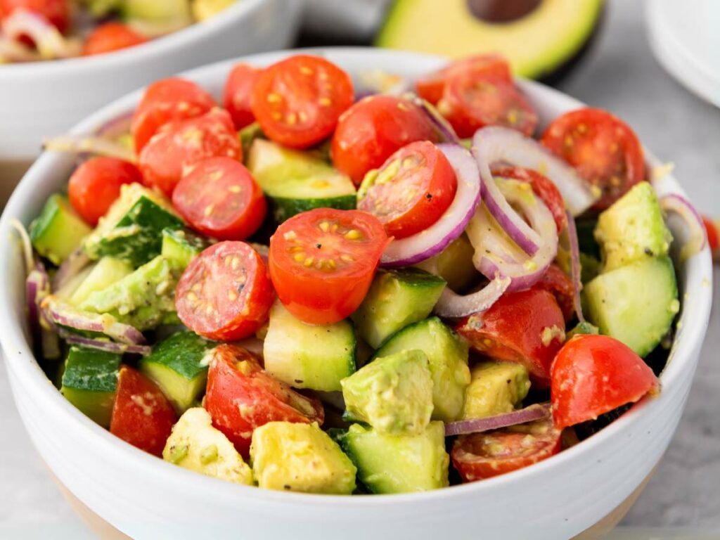 A bowl filled with avocado tomato salad with cucumber.