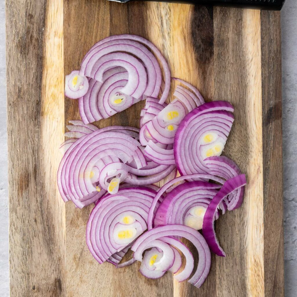 Thin slices of red onion arranged on a wooden cutting board.