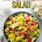 A bowl of chopped chicken salad with avocado, cherry tomatoes, lettuce, bacon, and cucumber, topped with black pepper.