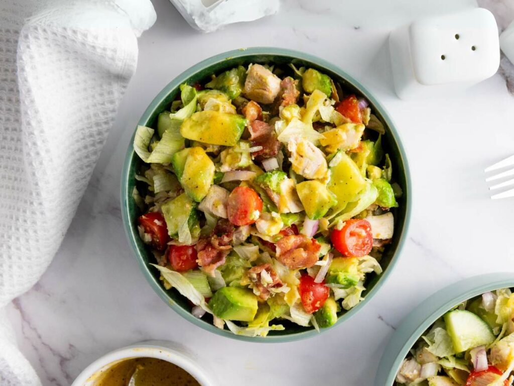 A bowl of chopped chicken salad placed on a white marble surface.