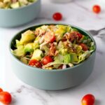 A bowl of chopped chicken salad, with whole cherry tomatoes scattered nearby.
