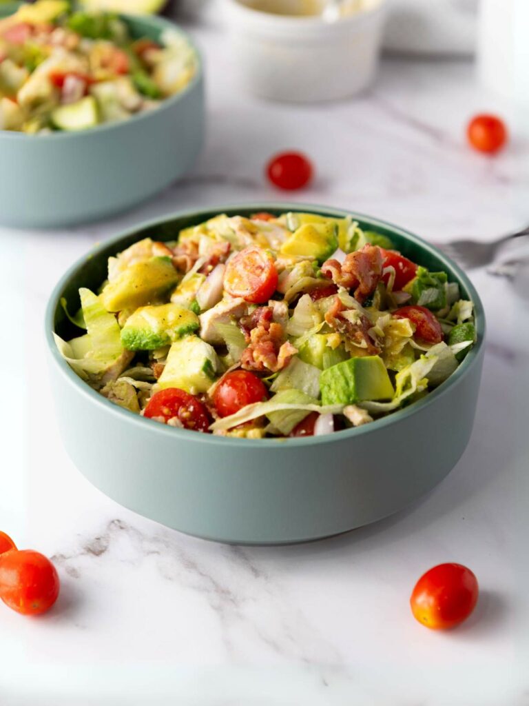A bowl of chopped chicken salad, with whole cherry tomatoes scattered nearby.