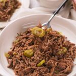 A white bowl filled with italian beef and sliced green peppers, with a fork lifting a portion.