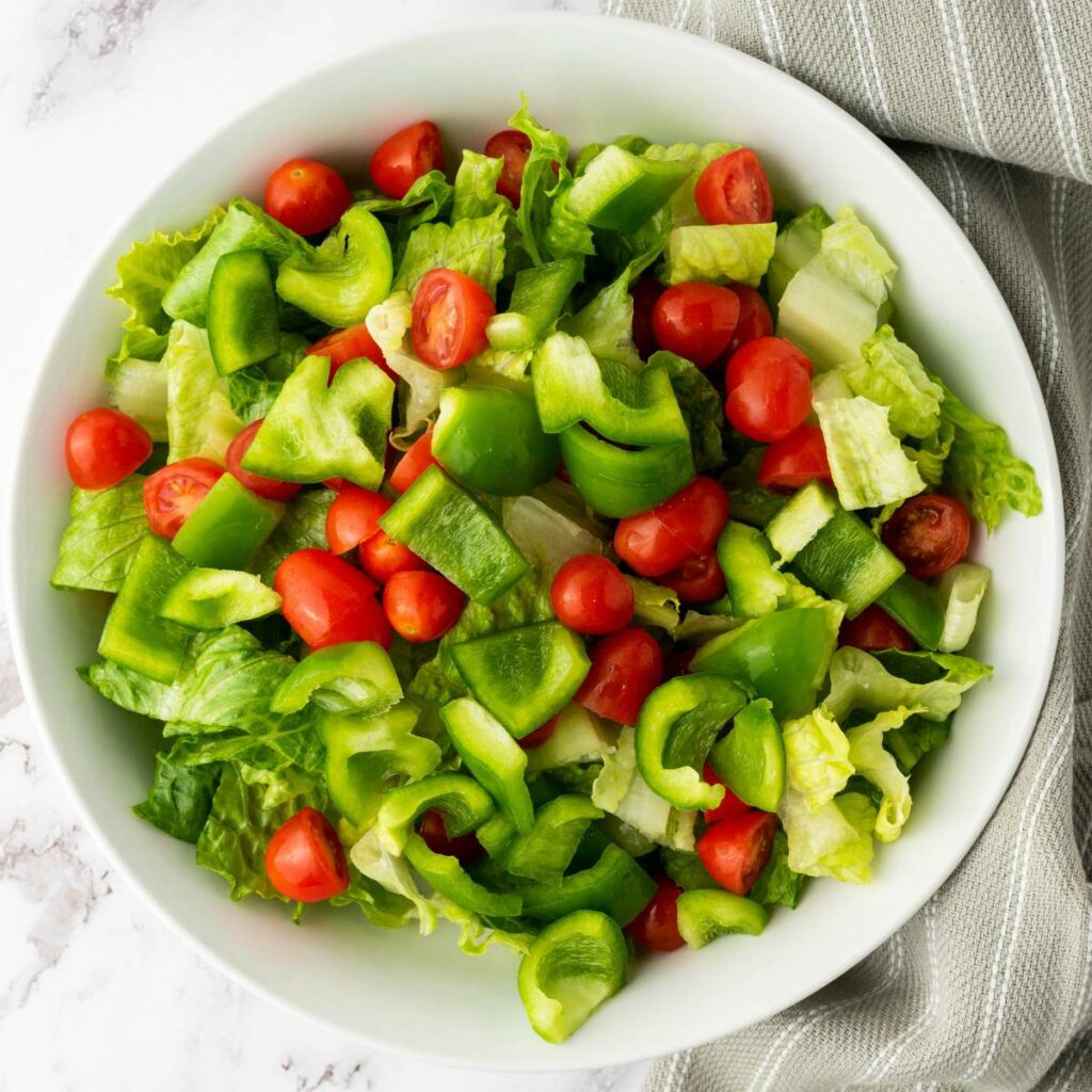 A white bowl filled with chopped lettuce, green bell peppers, and cherry tomatoes.