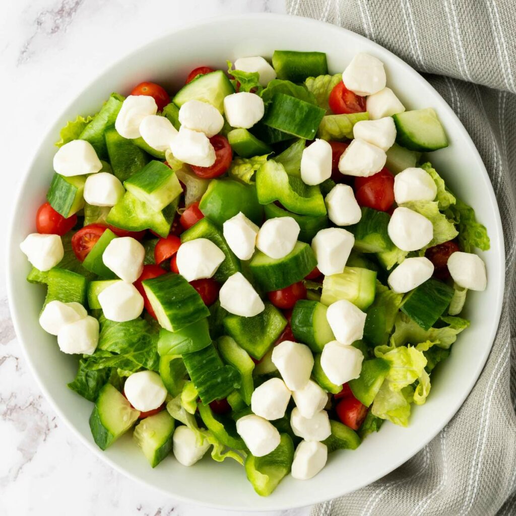 A bowl of salad with lettuce, cucumber, green bell pepper, cherry tomatoes, and mozzarella balls.