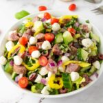 A bowl of italian chopped salad on a white colored surface.