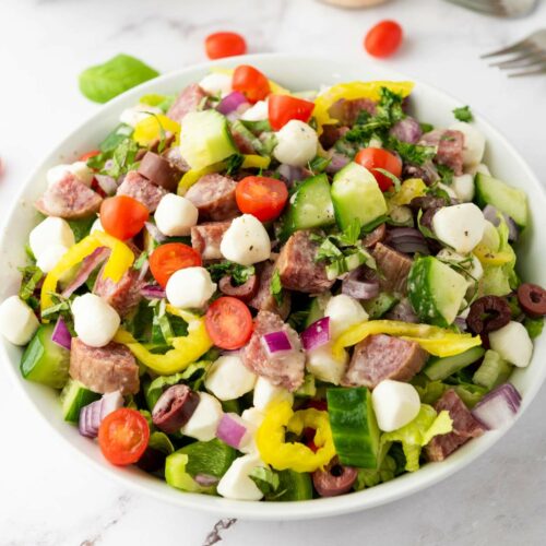 A bowl of italian chopped salad on a white colored surface.