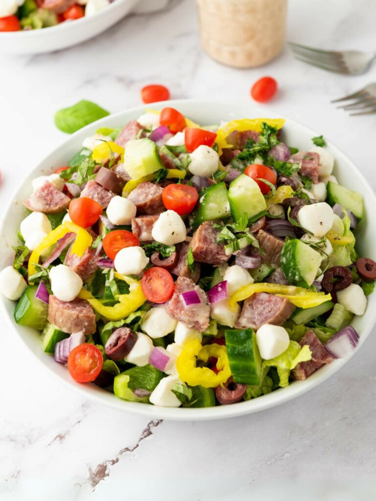 A bowl of italian chopped salad on a white colored surface.