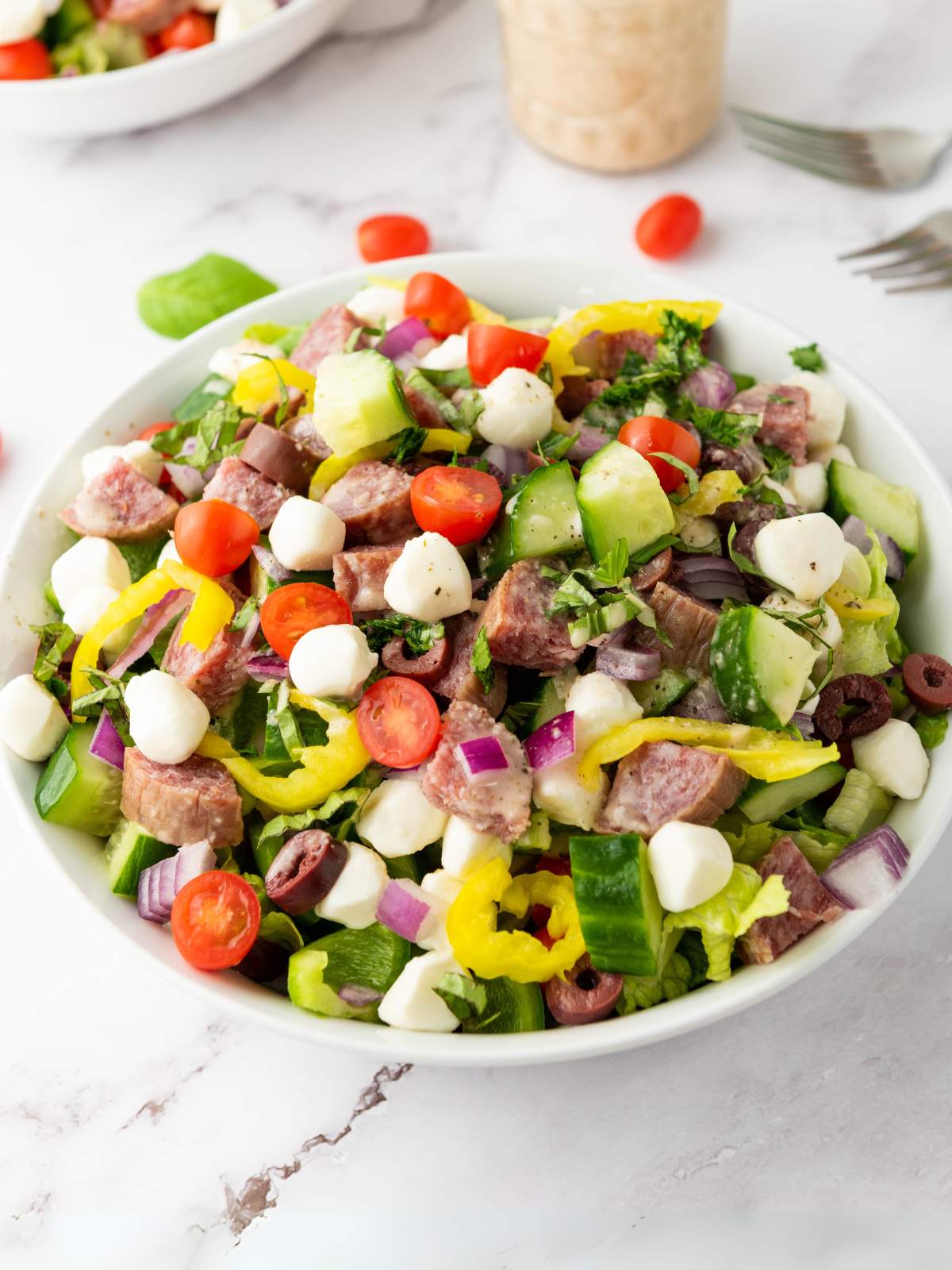 A bowl of italian chopped salad on a white colored surface.