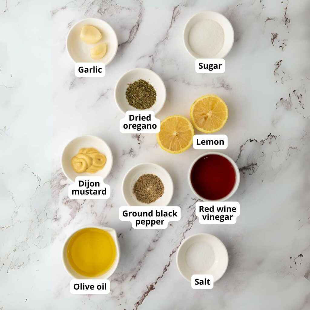 Nine ingredients for italian chopped salad dressing are arranged on a marble surface.