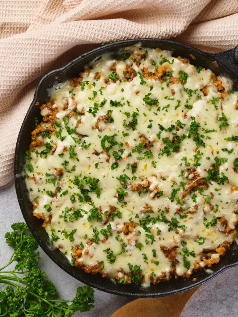 Italian ground beef skillet placed on a light surface with a towel and fresh parsley nearby.