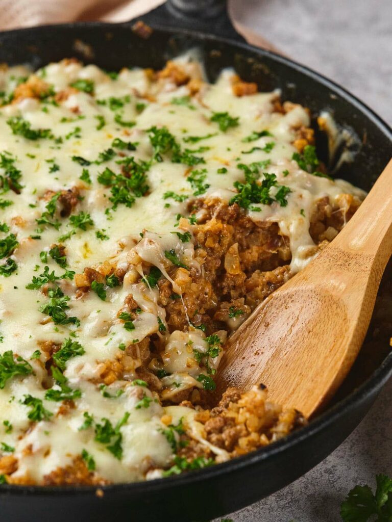 Italian ground beef skillet with a wooden spoon scooping a portion.