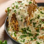 Italian ground beef skillet topped with melted cheese and chopped parsley, with a wooden spoon lifting a serving.