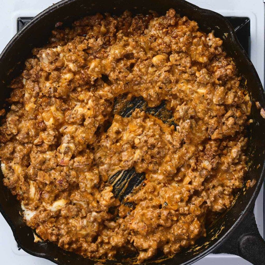 Ground meat cooked with sauce and melted cheese in a black cast iron skillet on a stovetop.