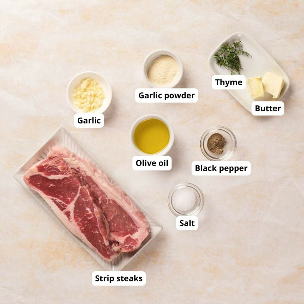 Raw strip steak, olive oil, chopped garlic, garlic powder, thyme, butter, black pepper, and salt.